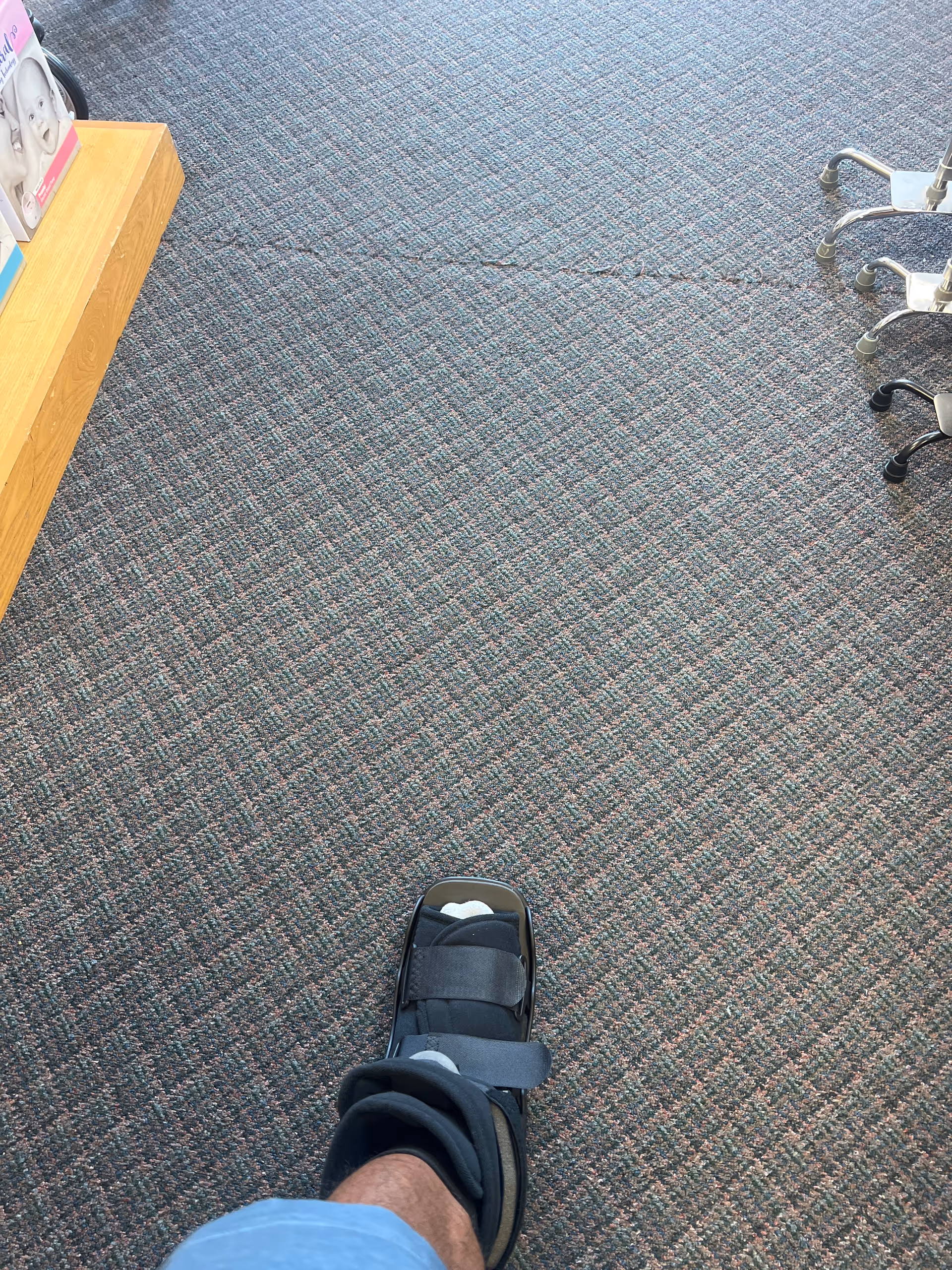 Person's foot in a medical boot on carpeted floor inside facility.