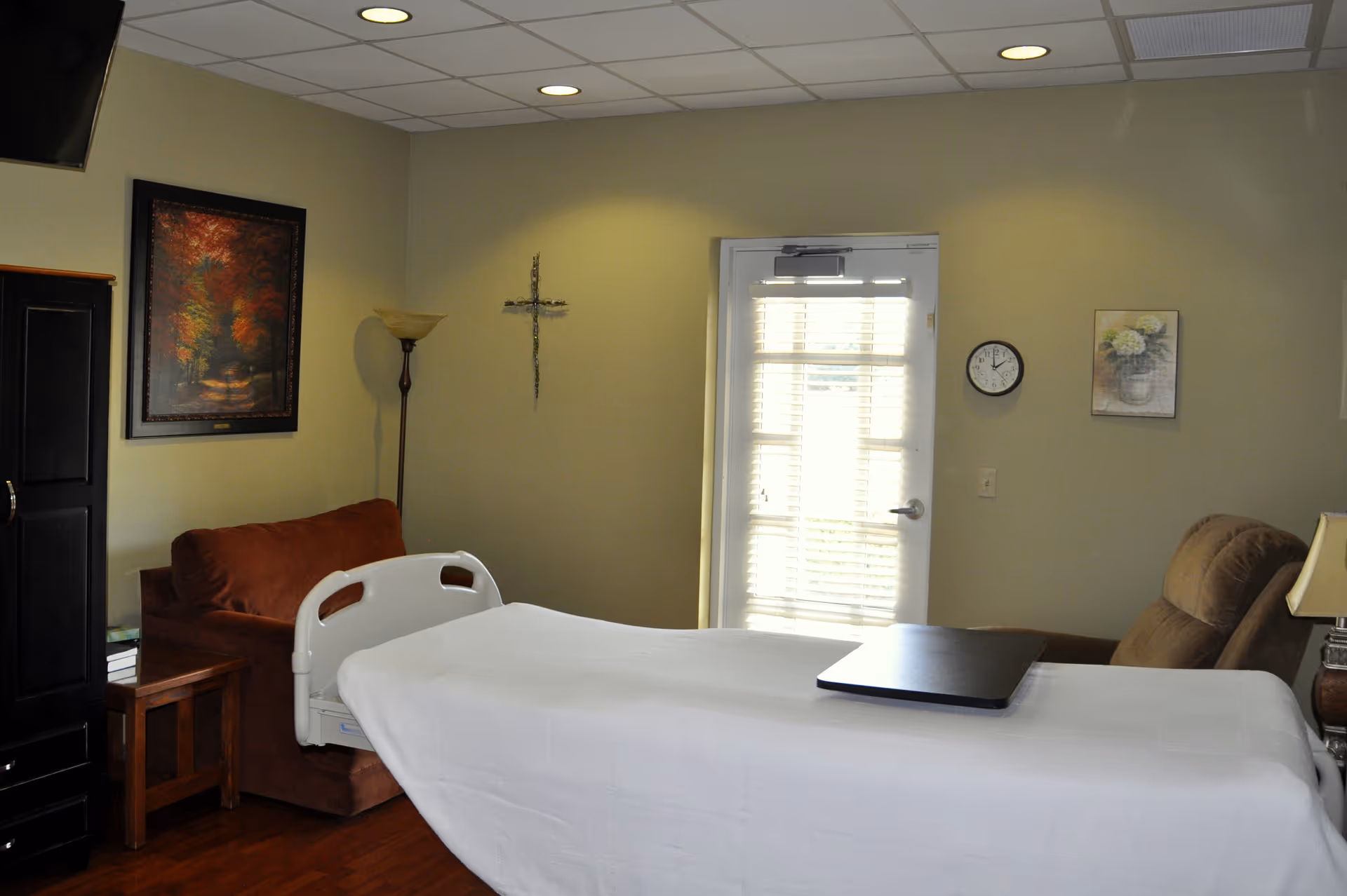 A resident room with a hospital-style bed, couch, and door with blinds.