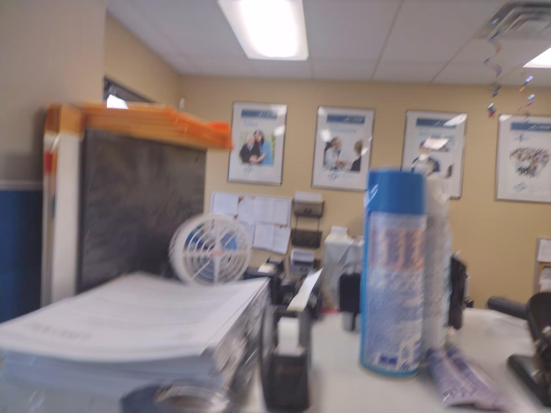 Reception desk inside a LINCARE facility with papers, a fan, and a tall blue bottle.
