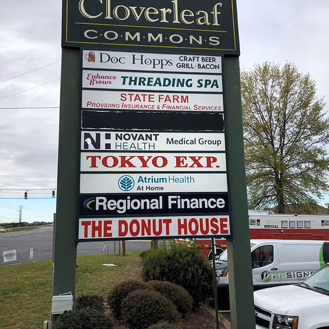 Tall outdoor signboard displays multiple business signs including Atrium Health At Home near busy traffic today.