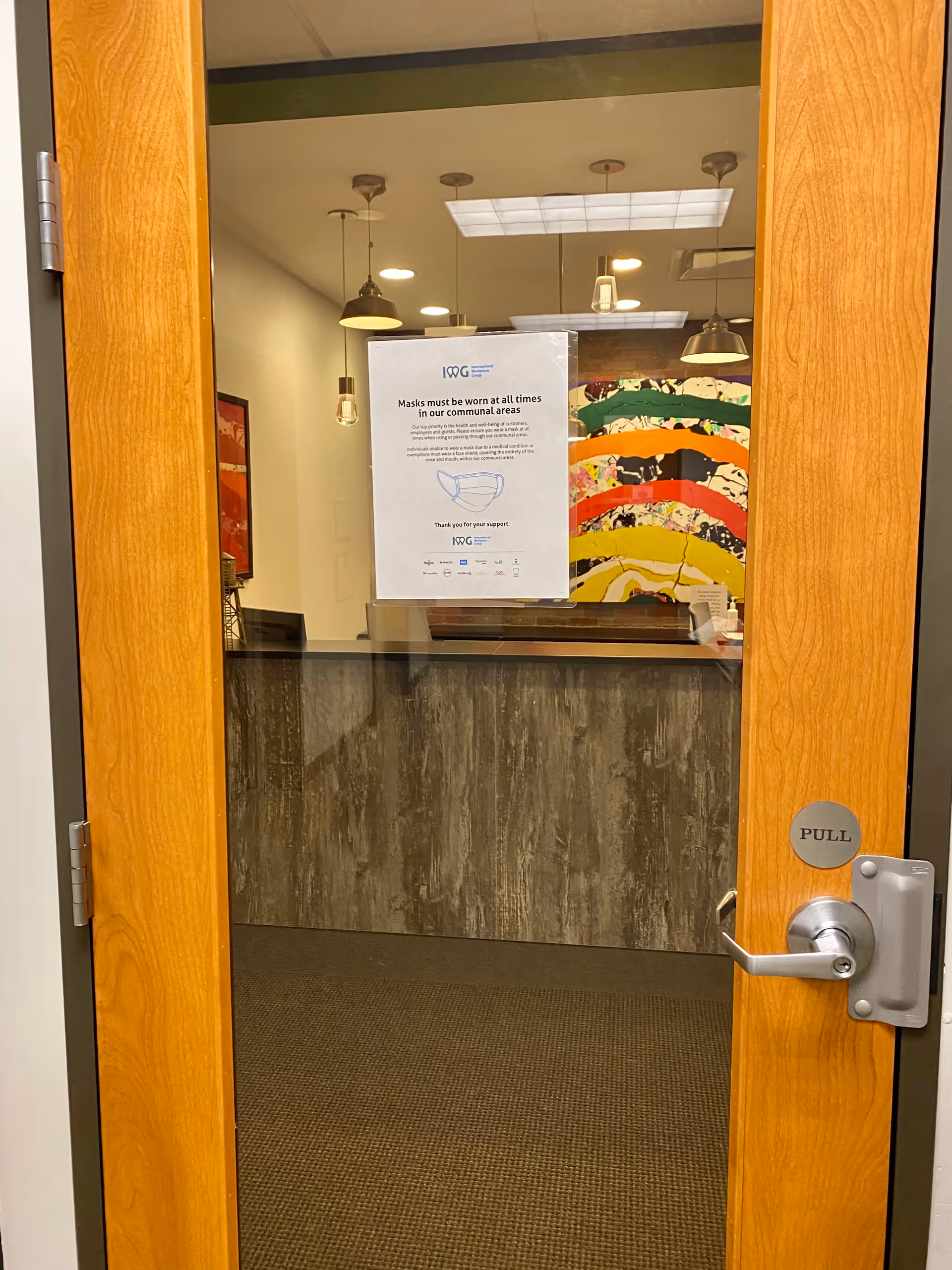 Wood-framed glass door opens to a reception desk in a dimly lit lobby.