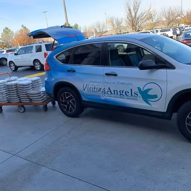 Visiting Angels van parked in a lot beside a cart of stacked plates.