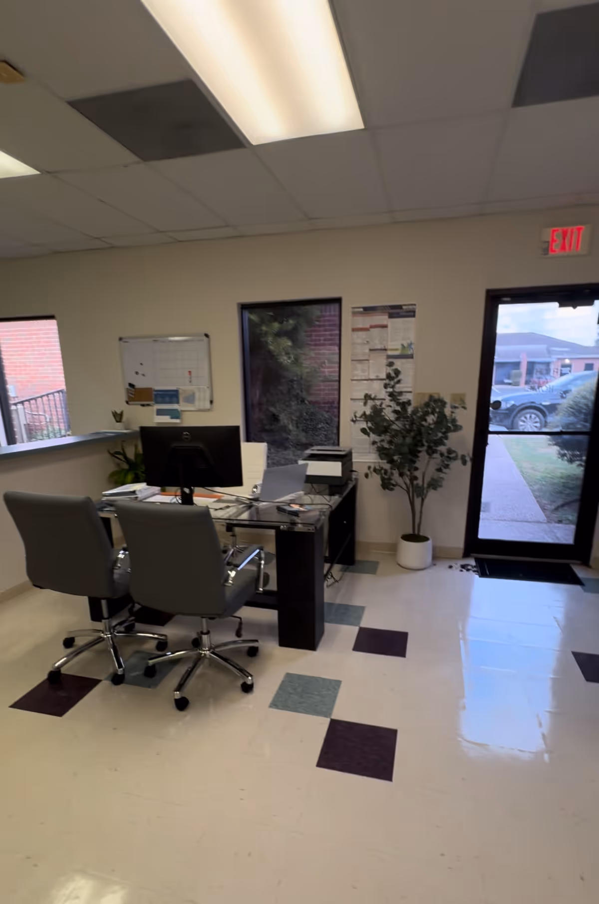 Office reception area inside a senior living facility with desk, computer, chairs, and exit door.