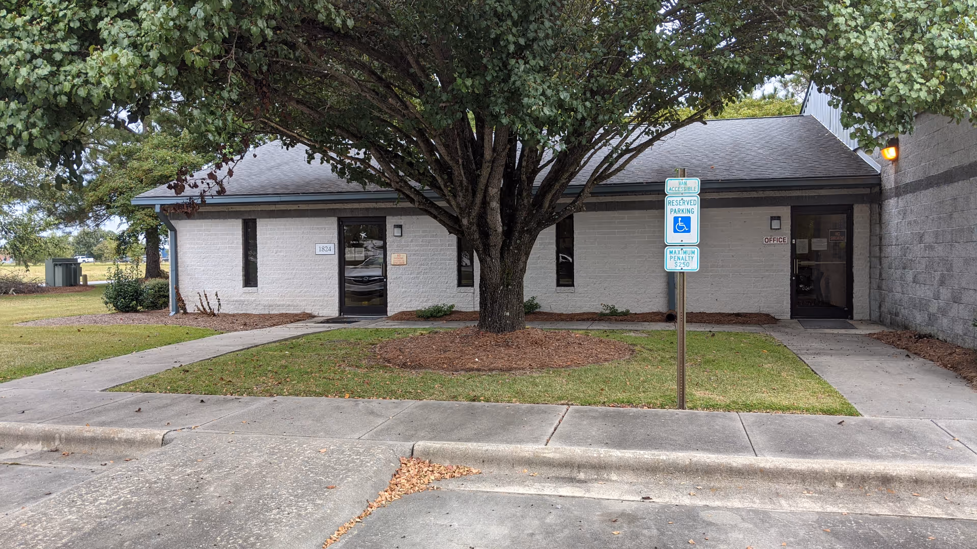 Apria Healthcare building exterior with a large tree, accessible entrance, and sidewalk.
