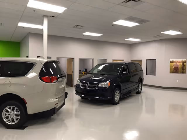 Indoor showroom with two minivans parked on a glossy floor under bright ceiling lights.
