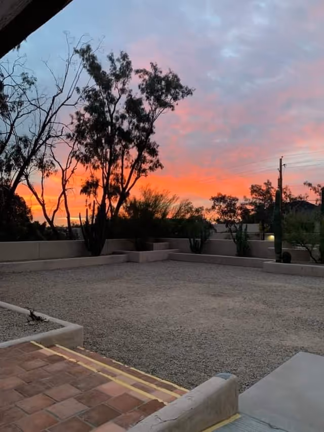Outdoor courtyard with gravel, low walls, and trees at sunset.