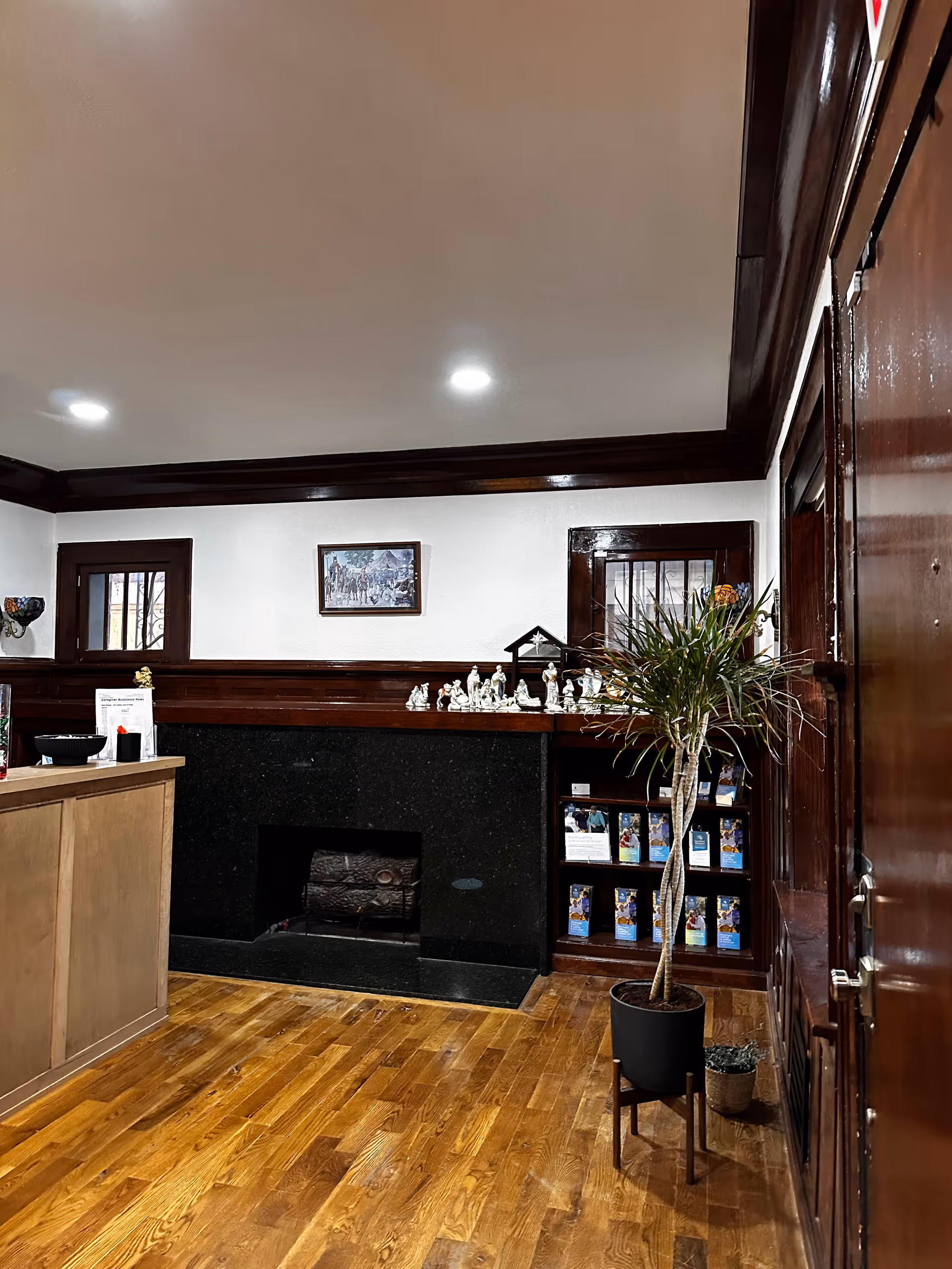Indoor facility lobby with wooden floors, fireplace, reception desk, plants, and shelves.