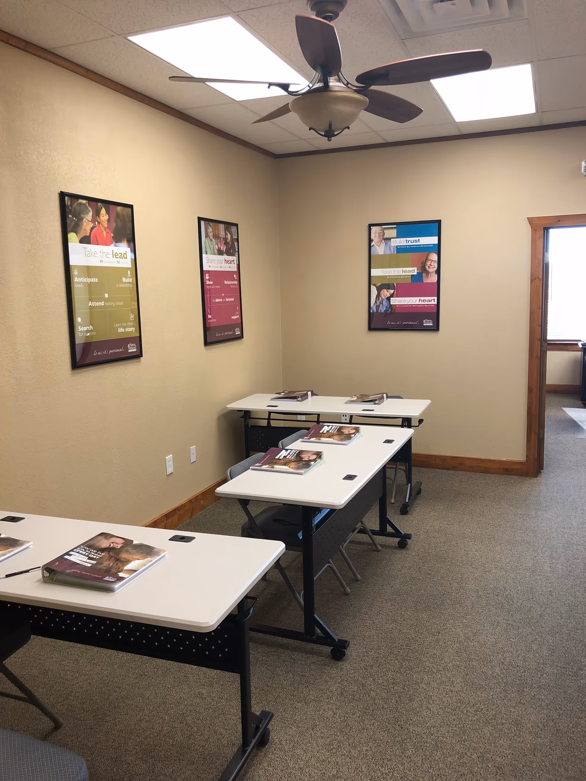Interior room with white tables, pamphlets, wall posters, and a ceiling fan.