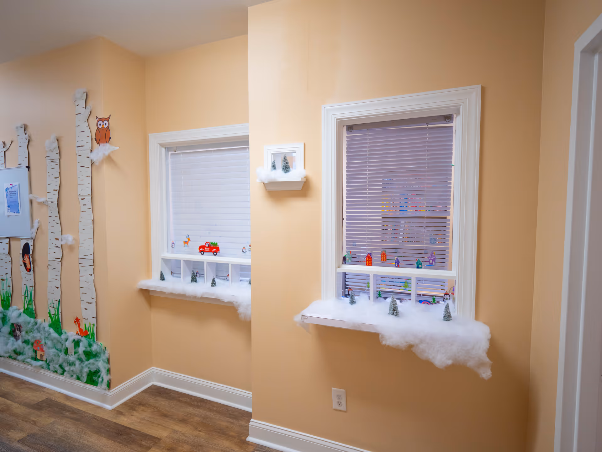 Two windows showcase winter crafts with cotton snow on a beige interior wall.
