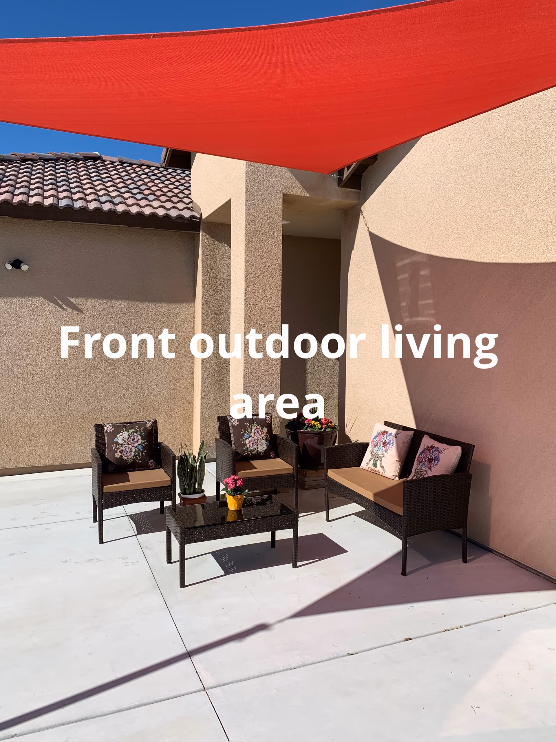 Front outdoor living area with wicker seating, glass table, cushions, and a red canopy.