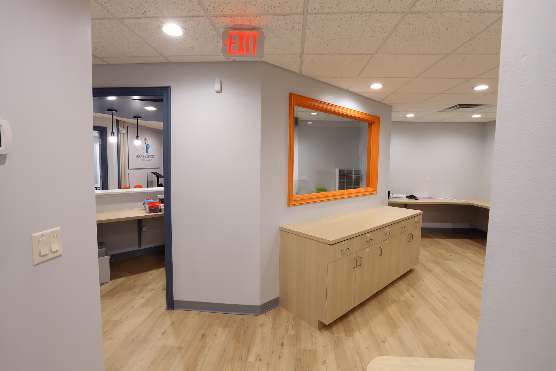 Interior hallway with wood flooring, orange-framed window, cabinets, and an EXIT sign.
