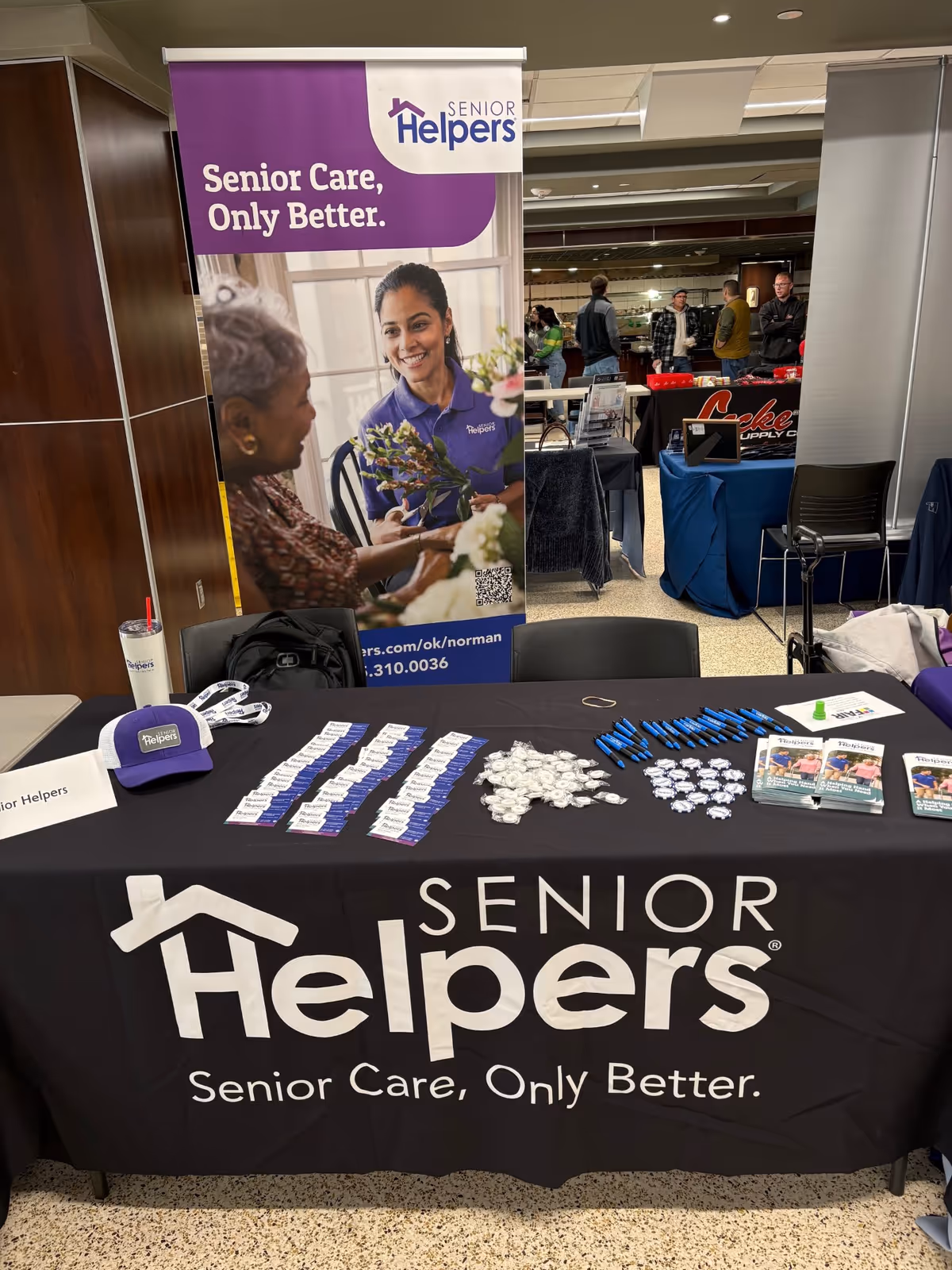 Promotional booth for Senior Helpers with banner, table, and brochures in a conference hall.