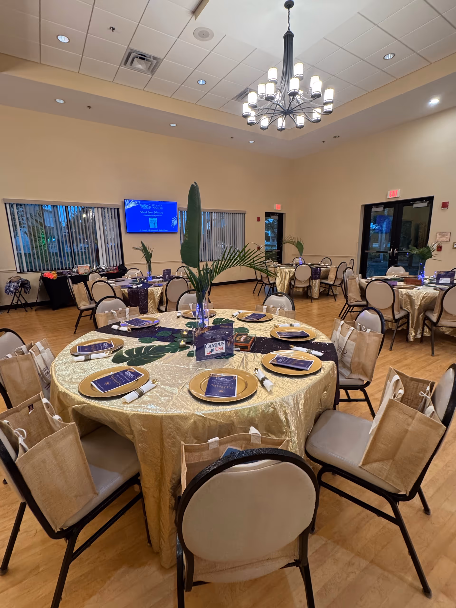 Round tables with gold tablecloths set for a meal in a spacious dining room.