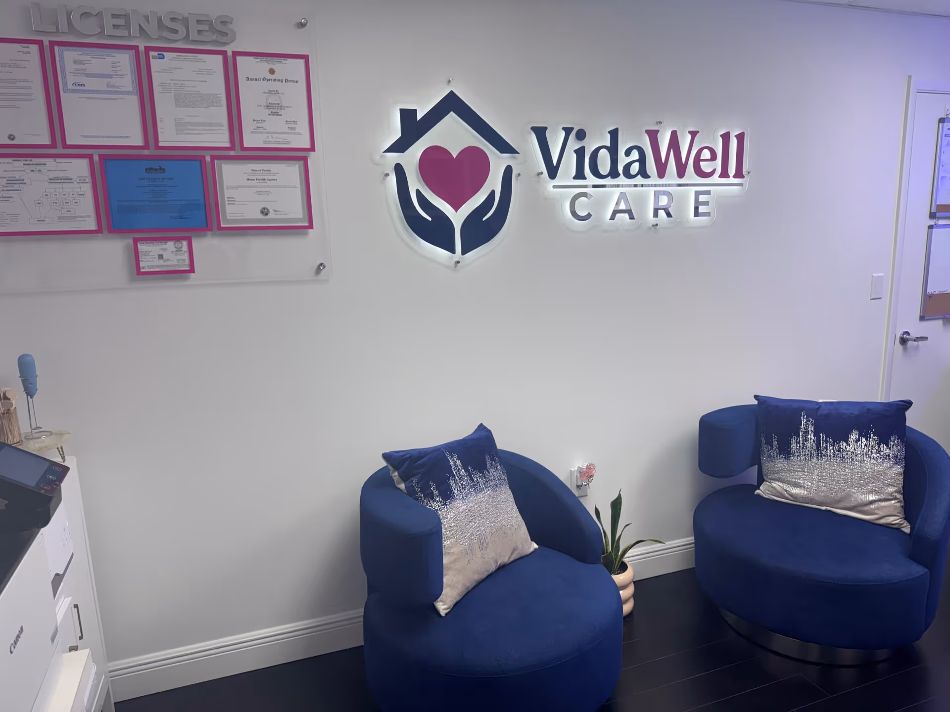 Reception area with blue chairs, a plant, and the VidaWell Care logo on the wall.