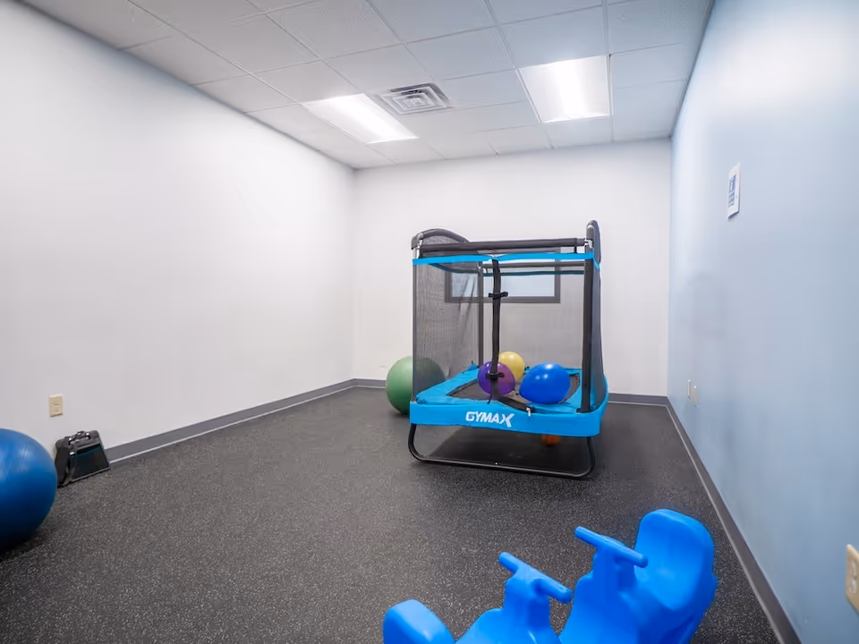 Indoor therapy room with a small trampoline, exercise balls, and blue walls.