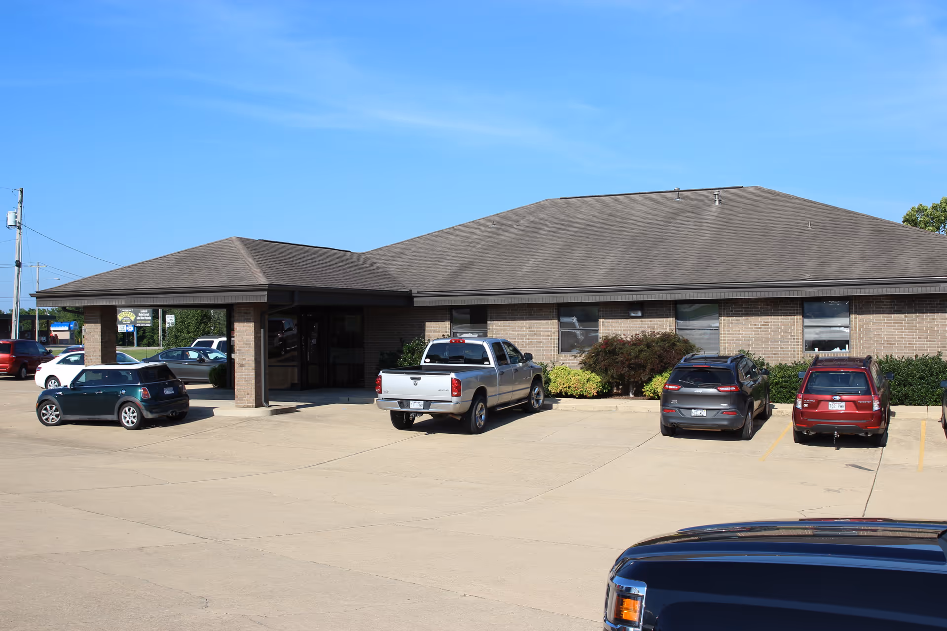 Exterior of a single-story brick facility with a front entrance and parked cars.