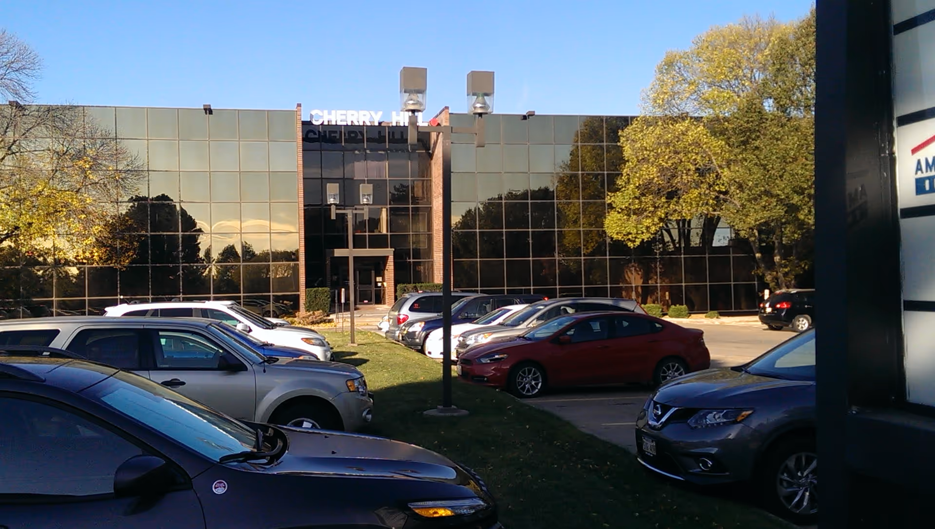 Glass-front building with a parking lot and trees under a clear blue sky.