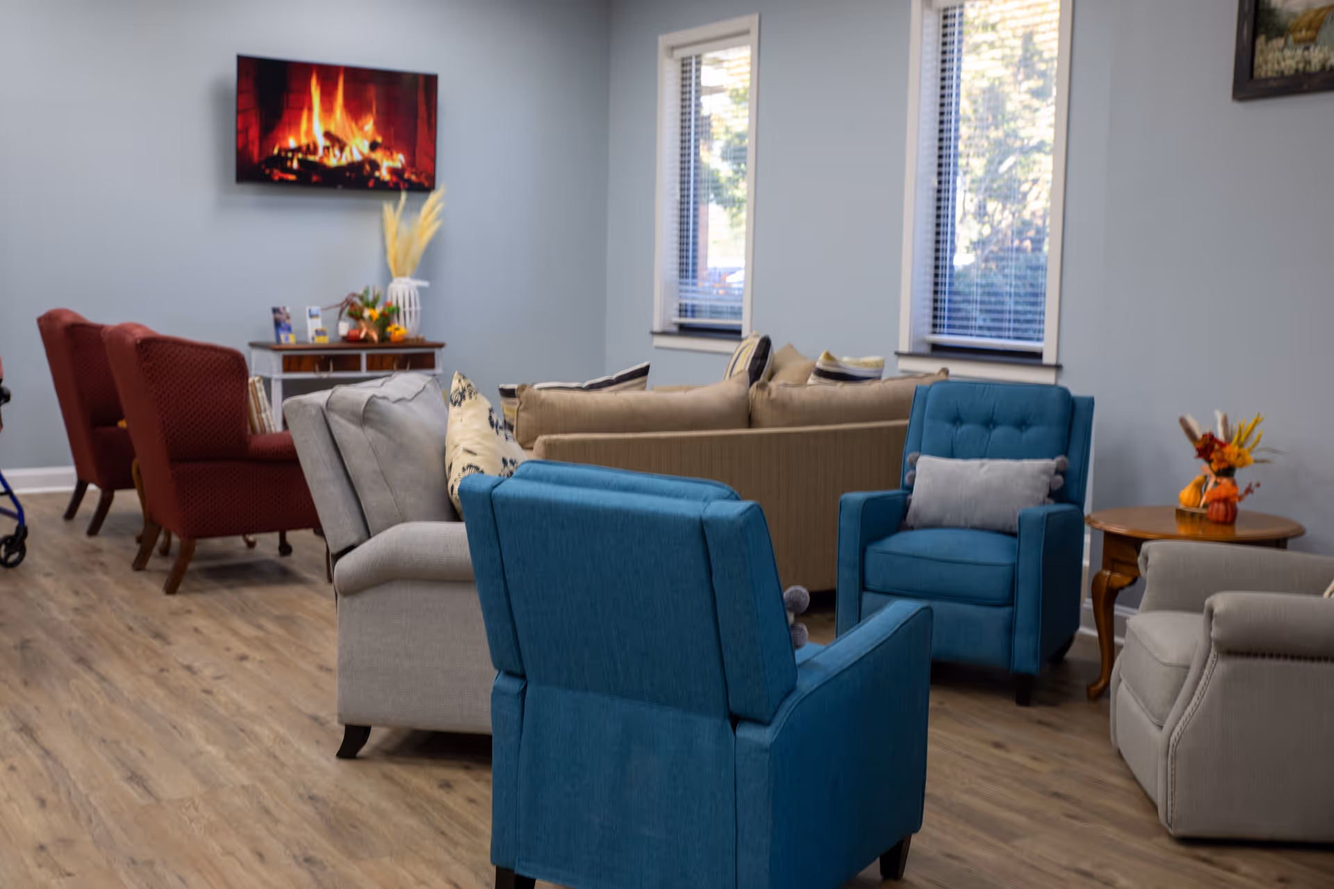 Cozy lounge with blue chairs, sofas, wooden floor, and a fireplace screen.