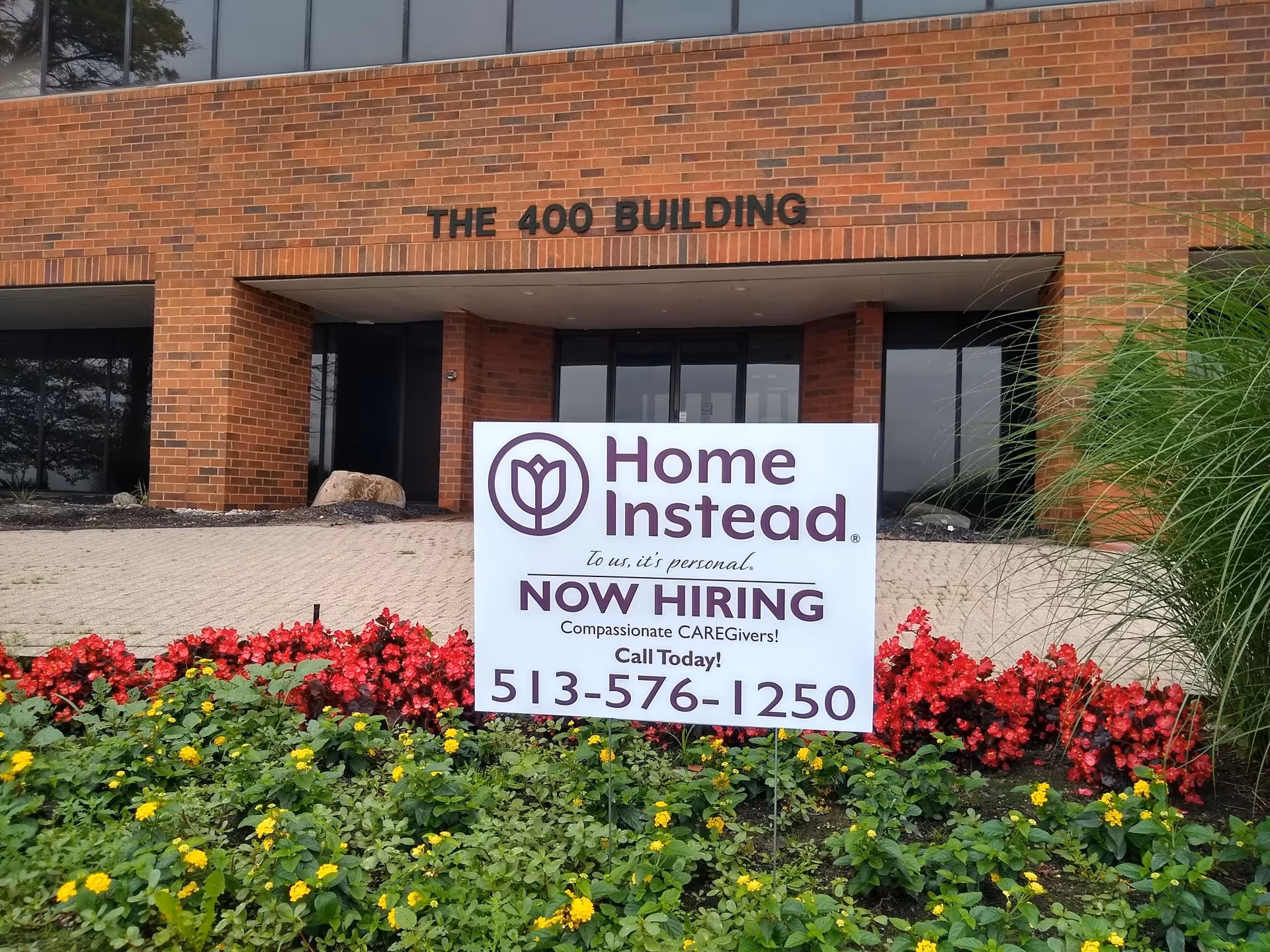 Front of a brick building with Home Instead sign and colorful flower beds.