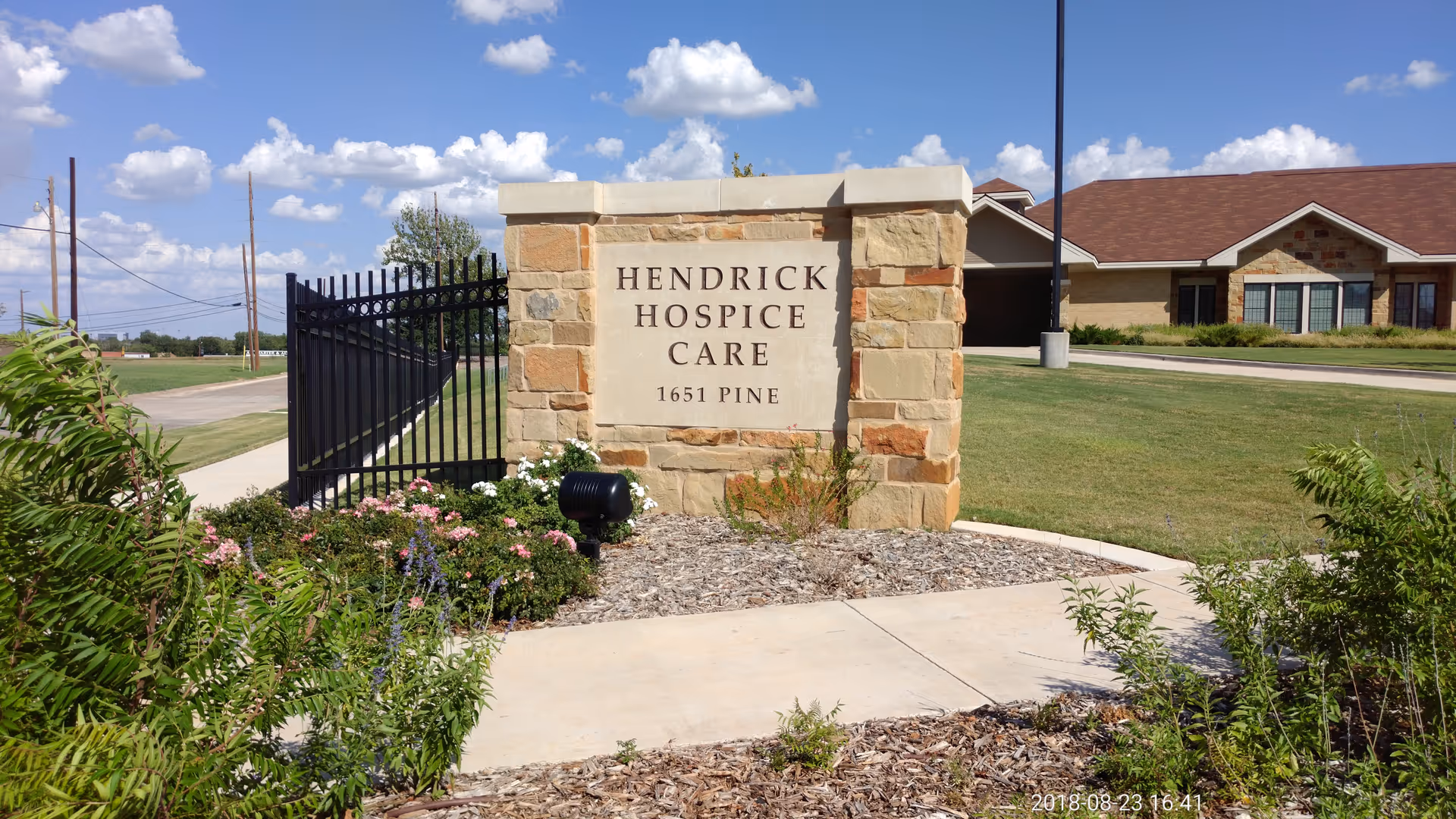 Stone sign reads Hendrick Hospice Care at a landscaped entry with a building in the background.