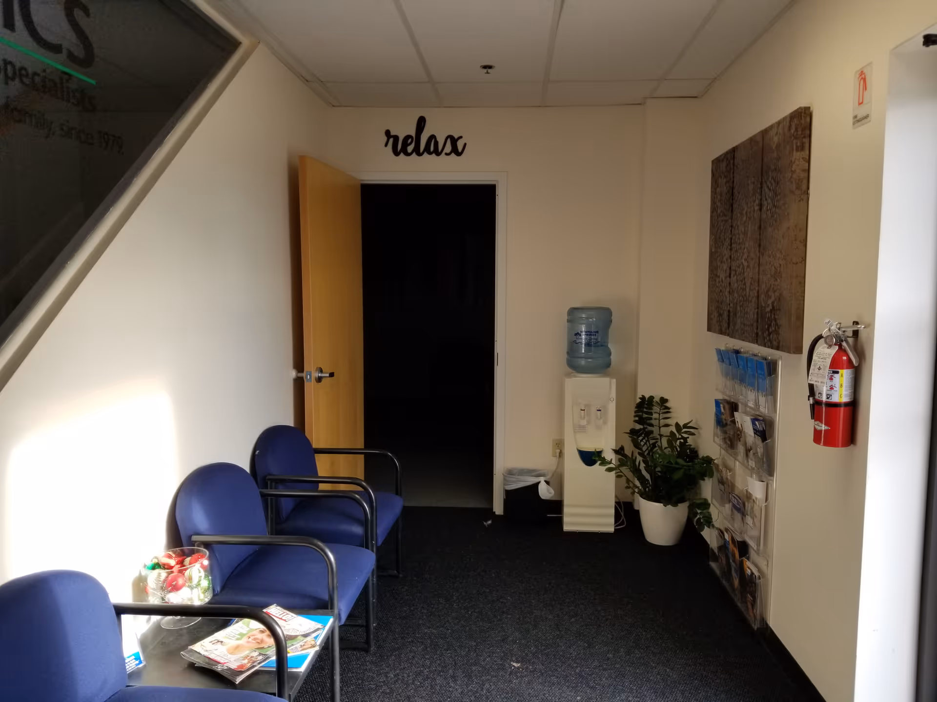 Interior waiting area with blue chairs, brochure rack, water cooler, and plants.