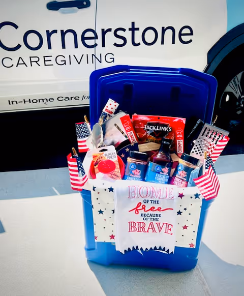 Patriotic gift bin with snacks and American flags beside a Cornerstone Caregiving van.