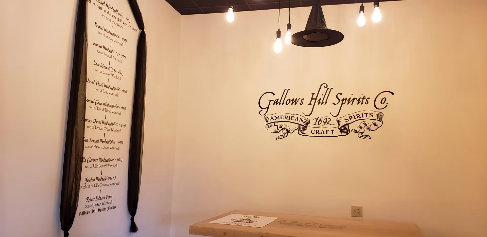Interior corner featuring wall graphic Gallows Hill Spirits Co and hanging light bulbs.
