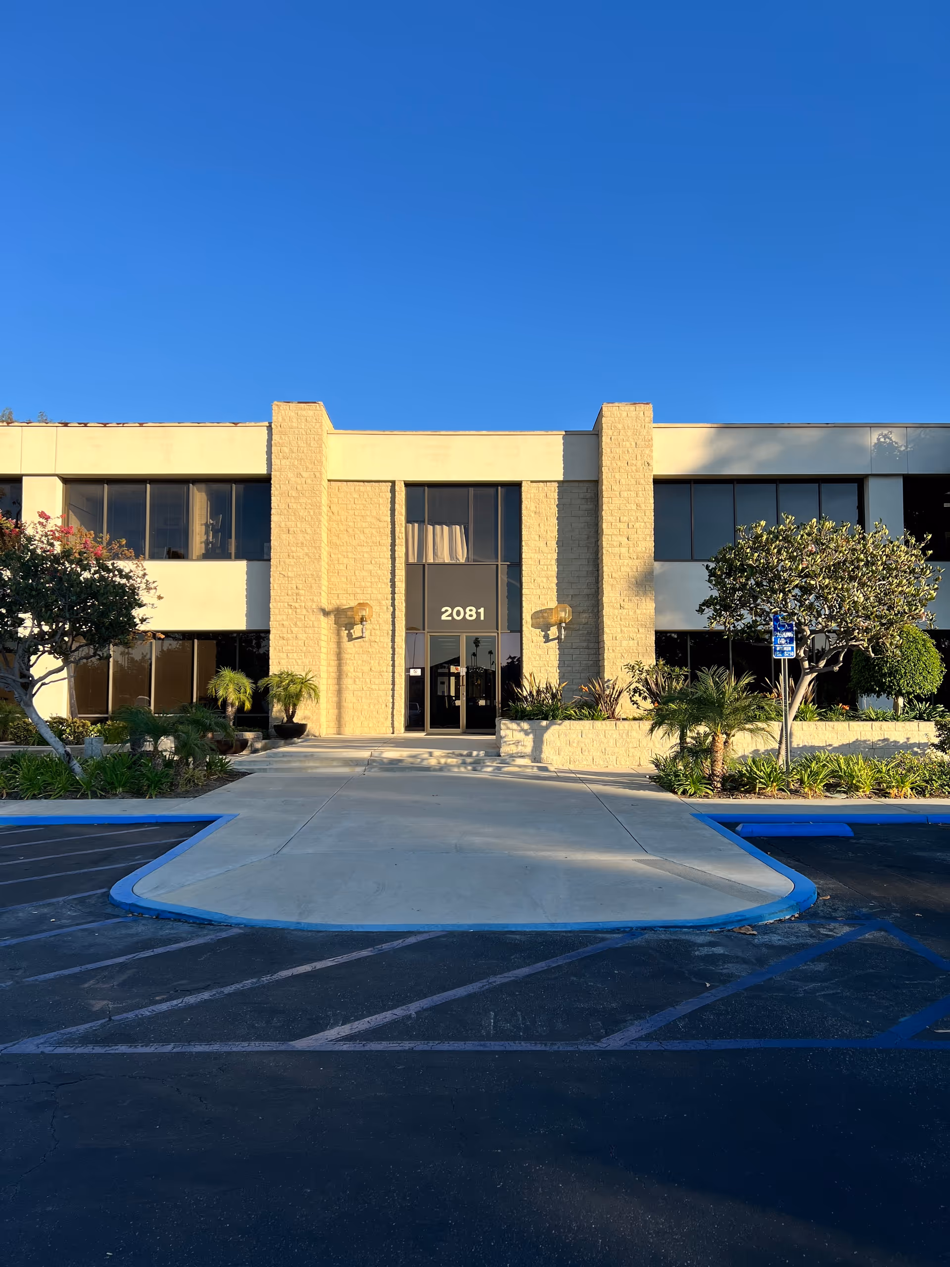 Exterior view of a senior living facility entrance with glass doors and a parking lot.