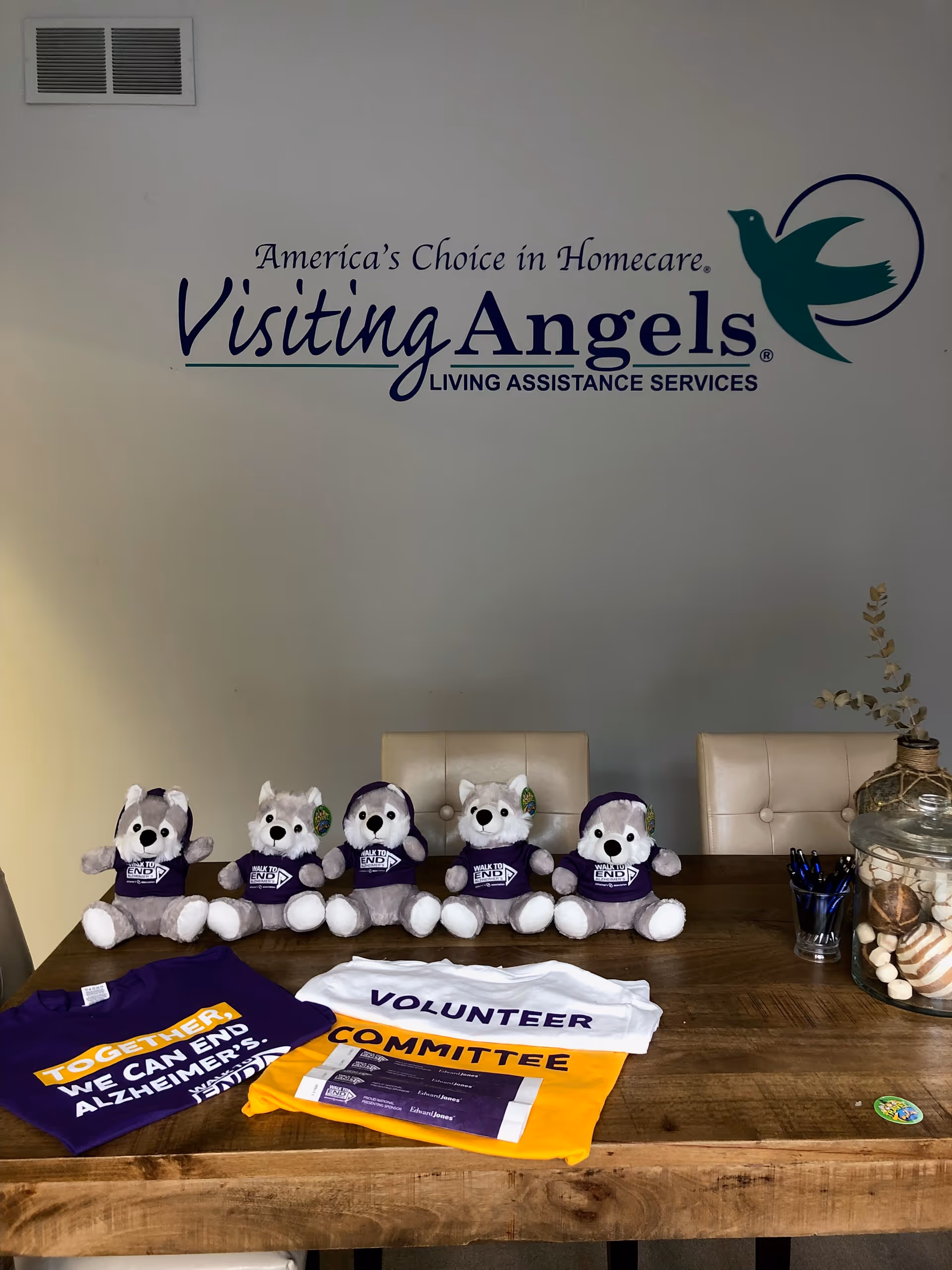 Indoor reception area featuring Visiting Angels logo and a table with volunteer shirts and plush dogs.
