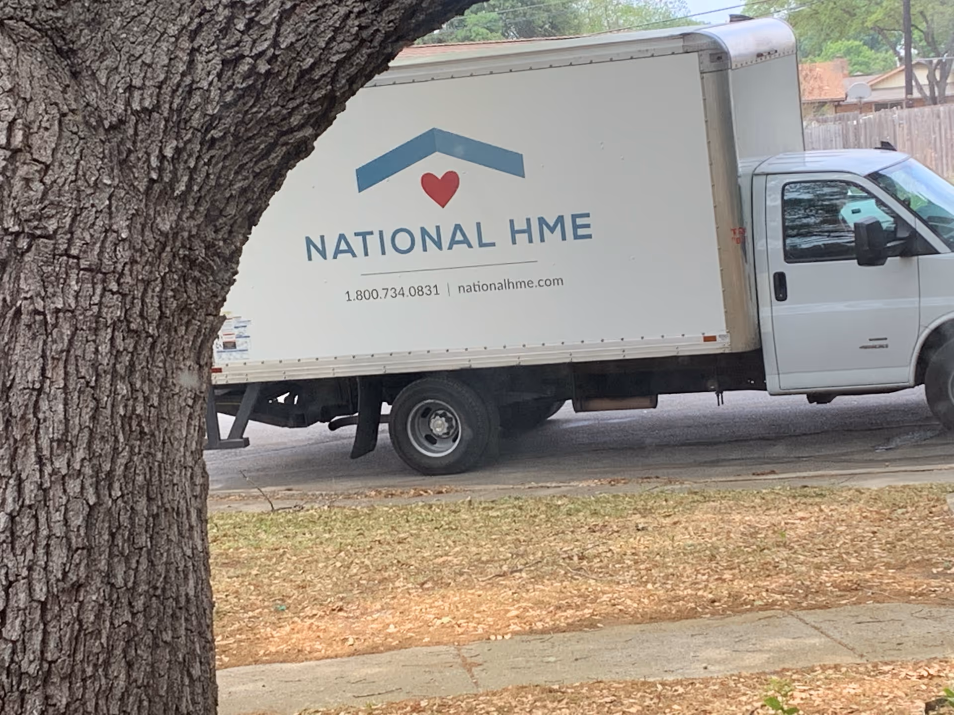 White National HME box truck parked on a street beside a large tree.