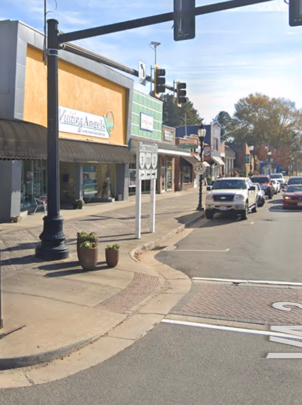 A street scene showing storefronts including Visiting Angels Senior Home Care and parked cars.