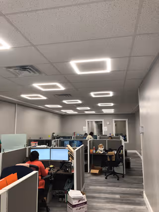 Office-like open workspace with cubicles, computers, and staff at desks inside a senior facility.