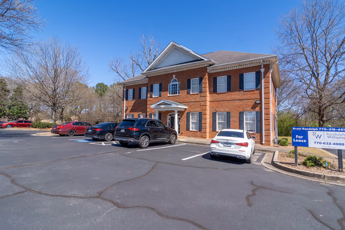 Two-story brick healthcare facility exterior with parked cars and blue sky.