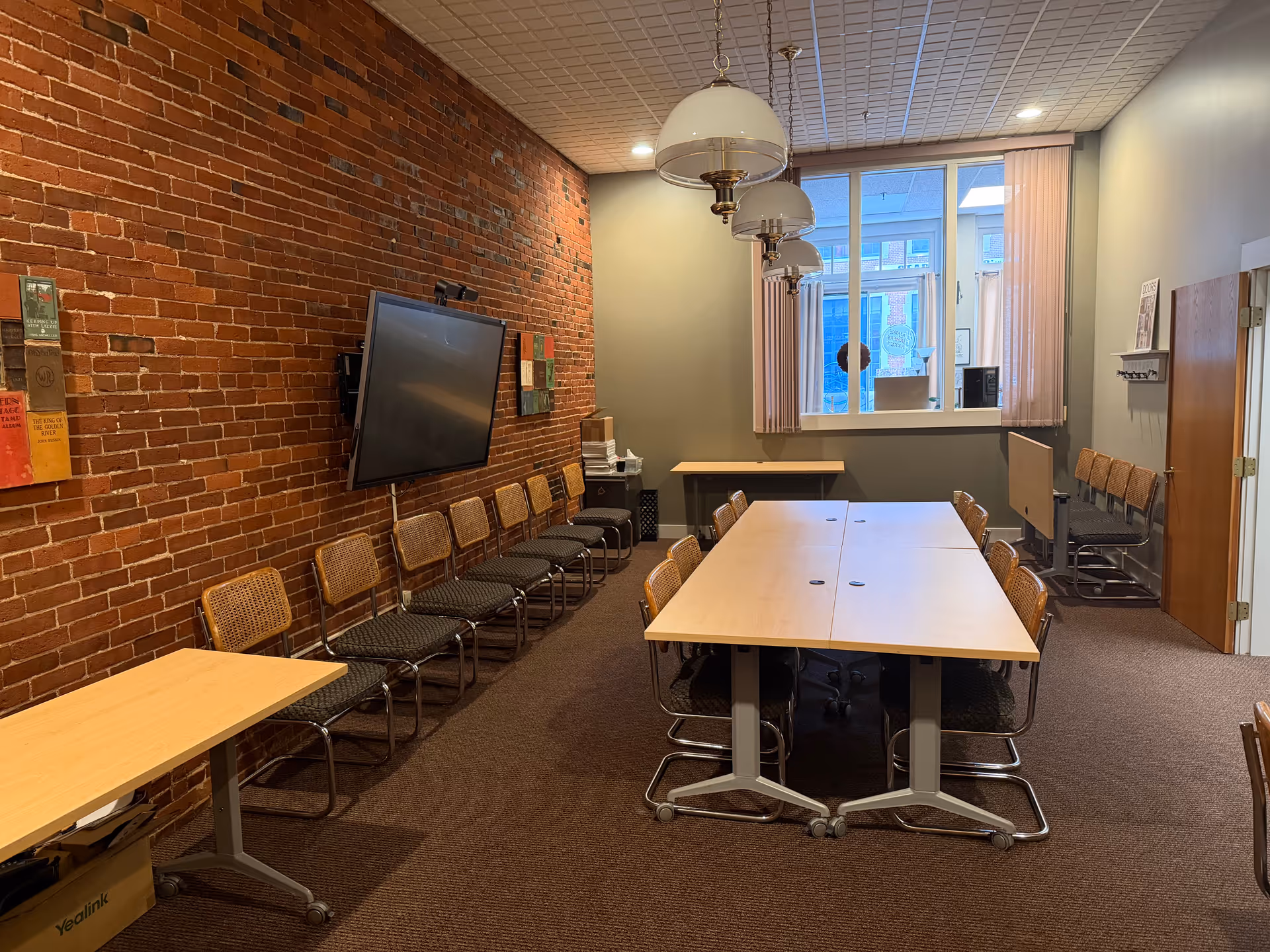 Brick-walled conference room with long tables, many chairs, a wall TV, and a large window.