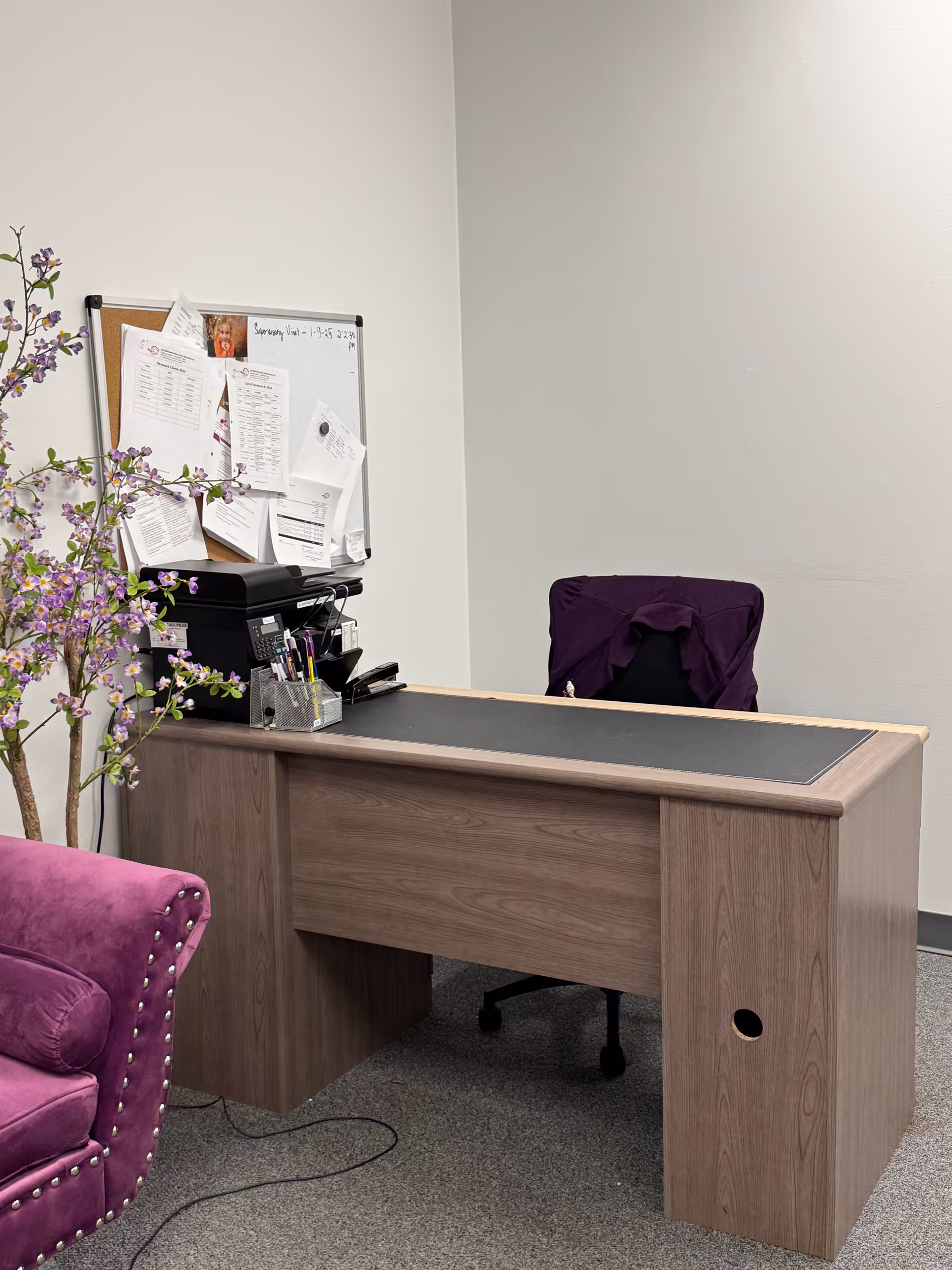 Wooden office desk with papers, a purple chair, and a purple sofa in a reception area.