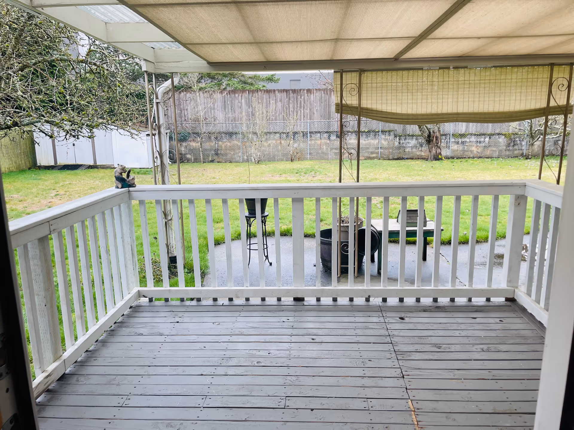 Covered wooden porch with railing, outdoor seating, and a grassy yard beyond.