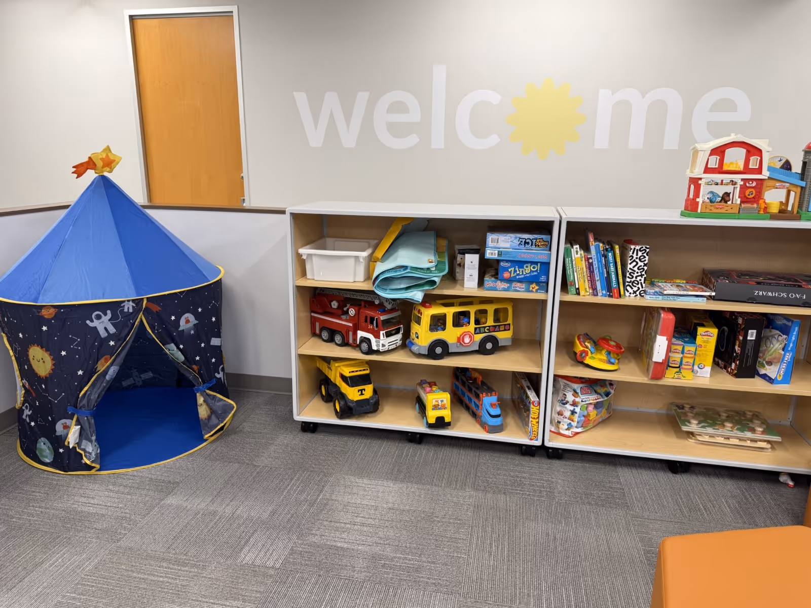 Interior play area with a blue tent, toy shelves, and a welcome sign.