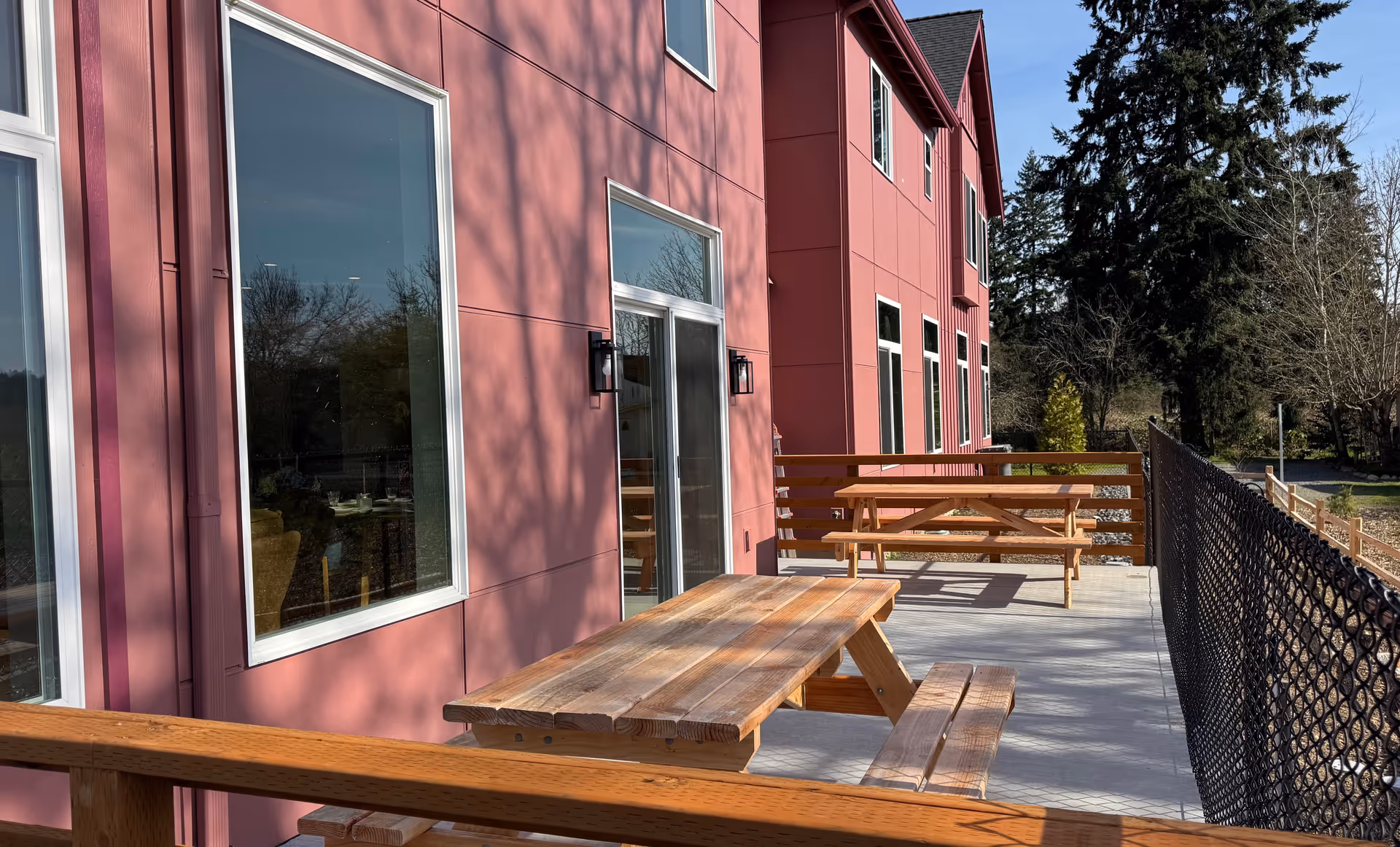 Pink, multi-story senior living building exterior with wooden picnic tables on a concrete outdoor patio.