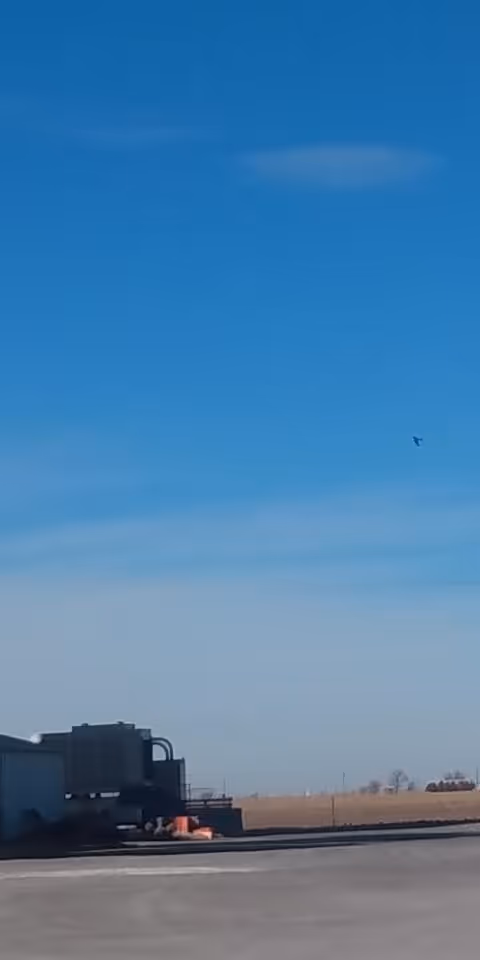 Blue sky over a facility exterior with industrial equipment and open field.