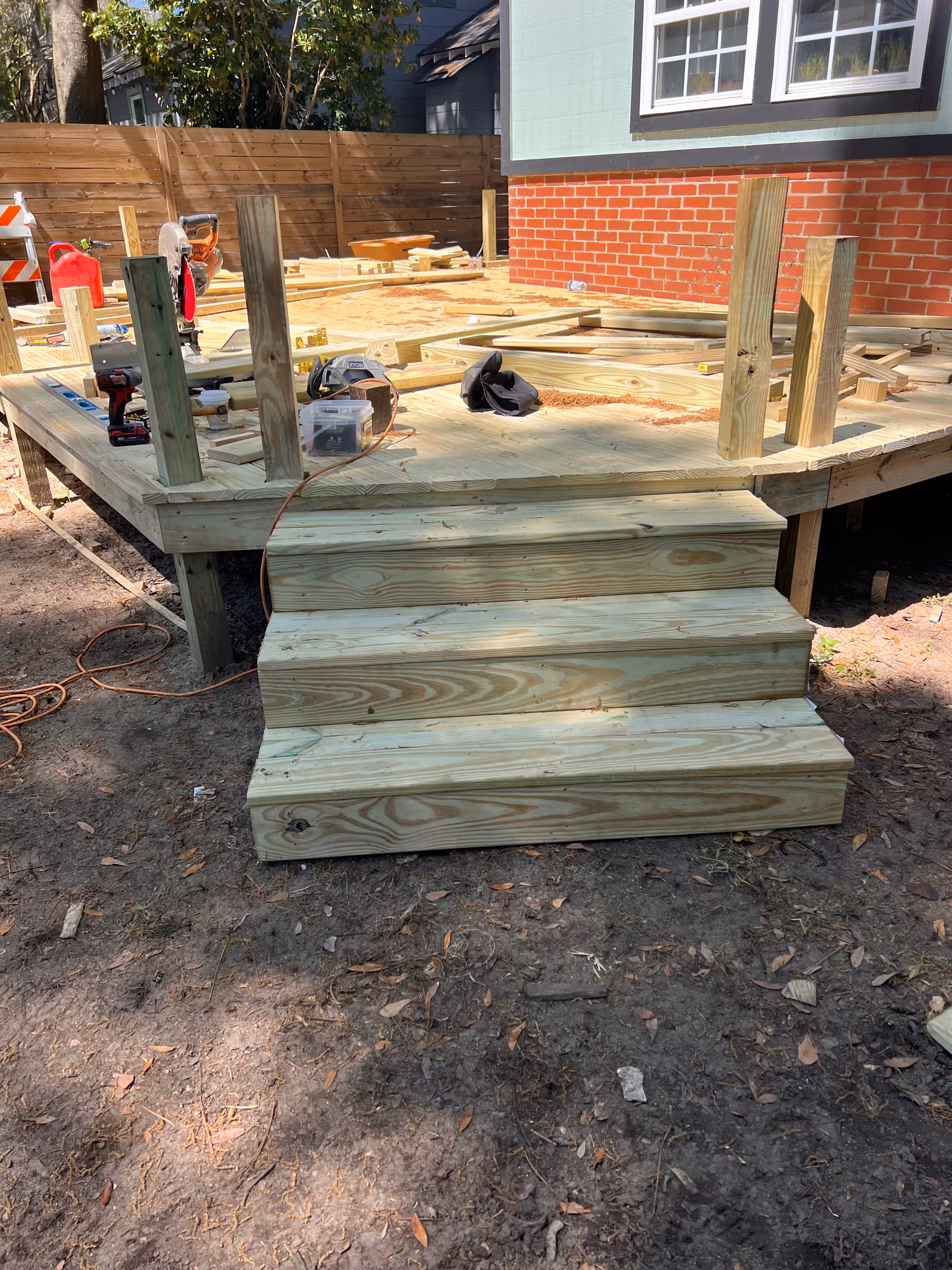 Unfinished wooden deck with stairs under construction outside a brick building.