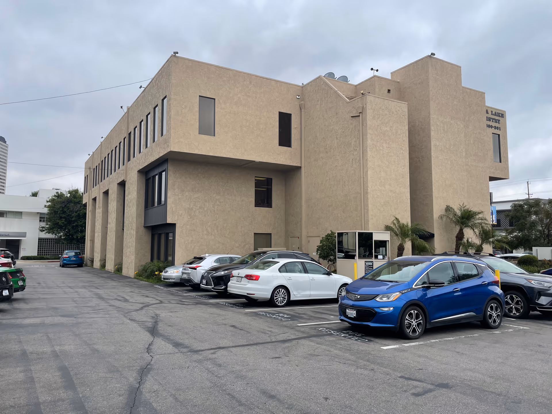 Two-story beige facility exterior with a parking lot and several cars in front.