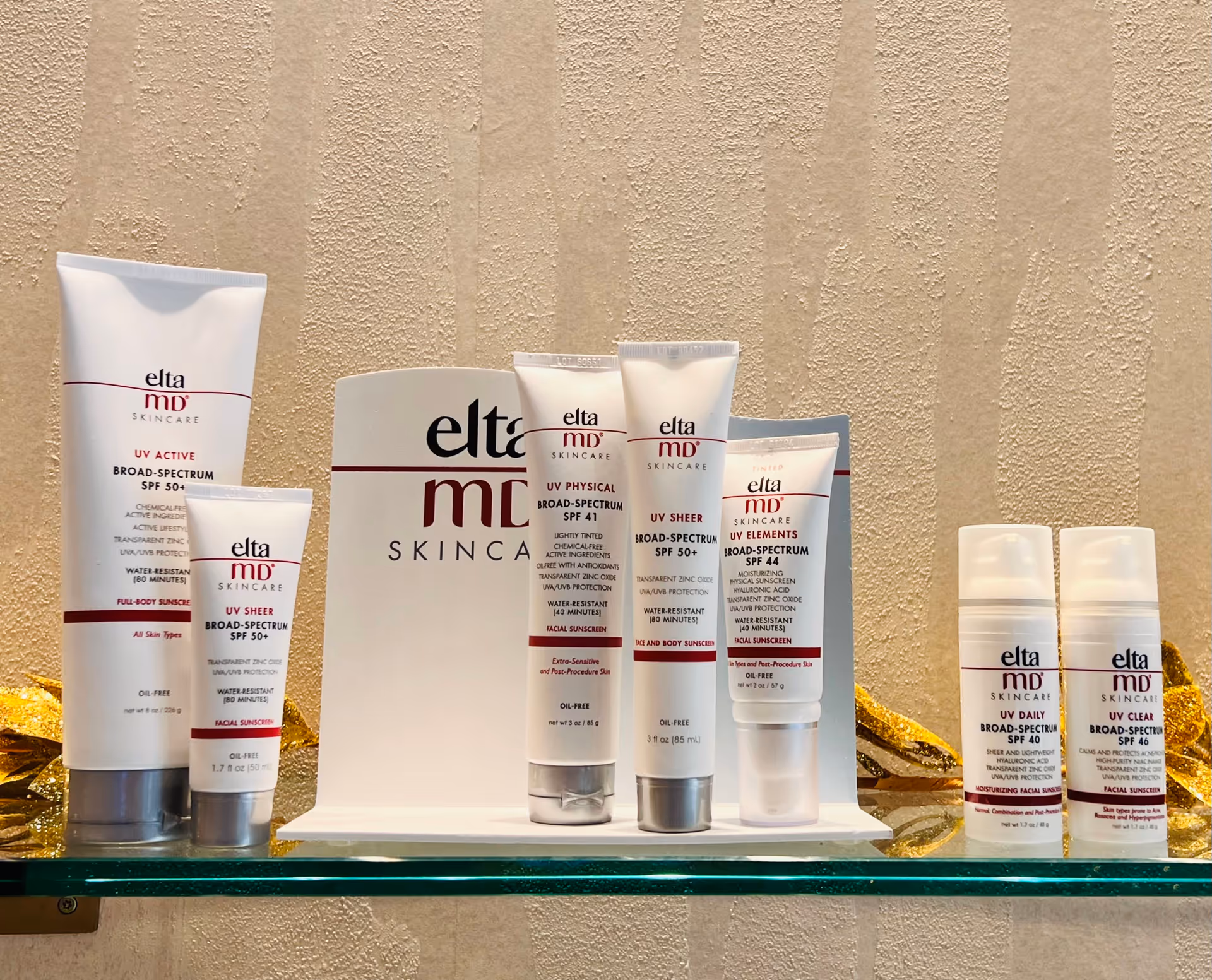 Assorted EltaMD skincare tubes displayed on a glass shelf against a beige wall.