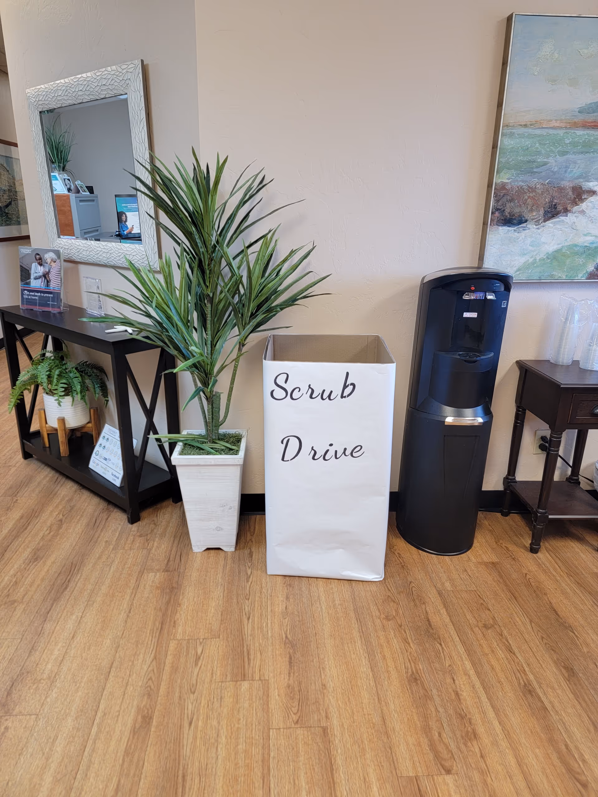 Interior lobby featuring a tall plant, a Scrub Drive bin, water cooler, mirror, and artwork.