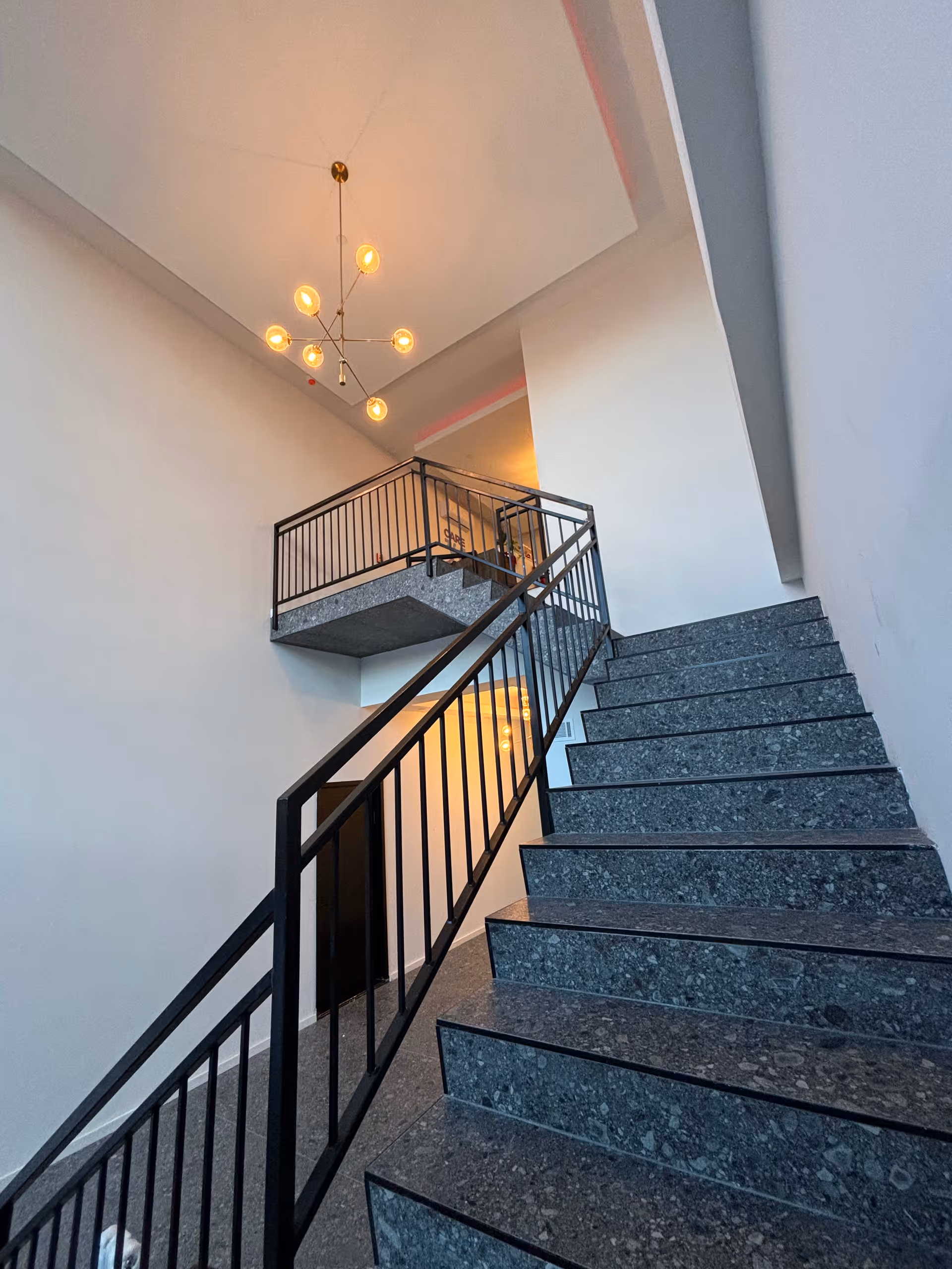 Modern indoor stairwell with metal railing, gray steps, and a hanging chandelier.