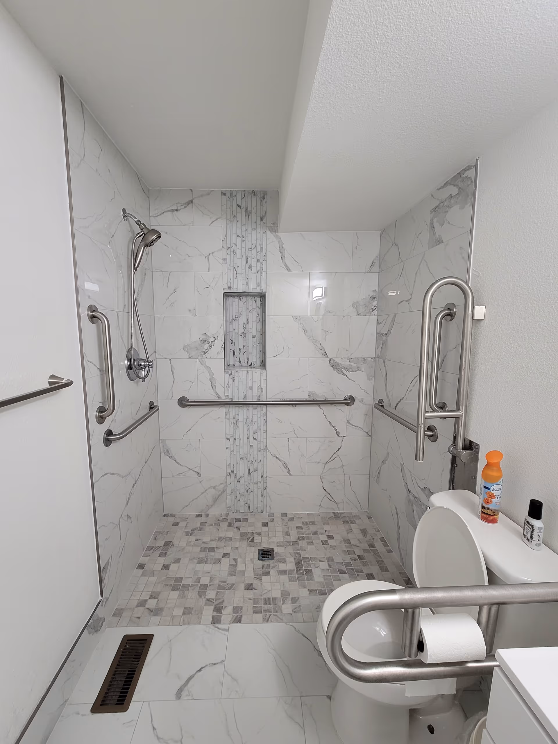 Accessible bathroom with tiled walk-in shower, grab bars, and a toilet in a senior facility.