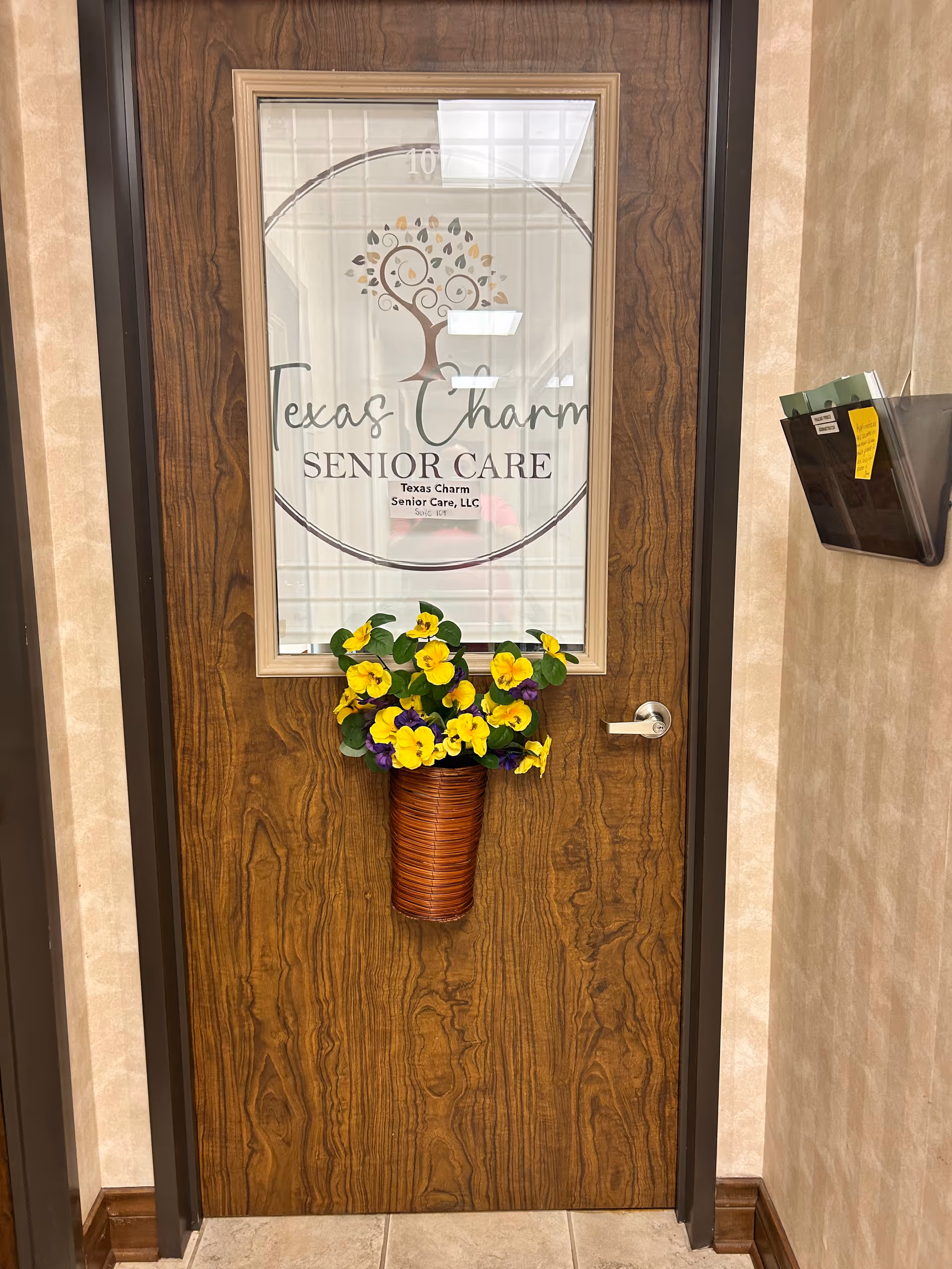 Wooden door bearing Texas Charm Senior Care logo and a flower arrangement