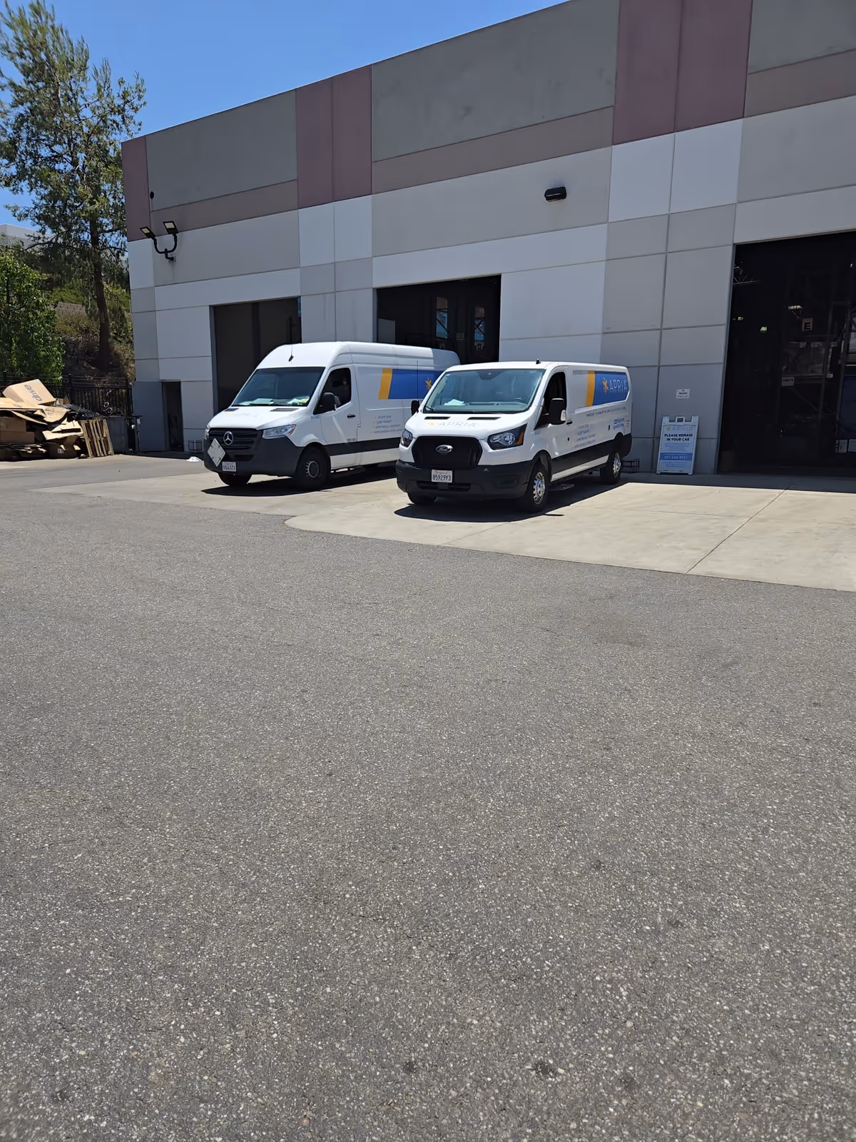 Two white delivery vans parked outside a modern building with large garage doors