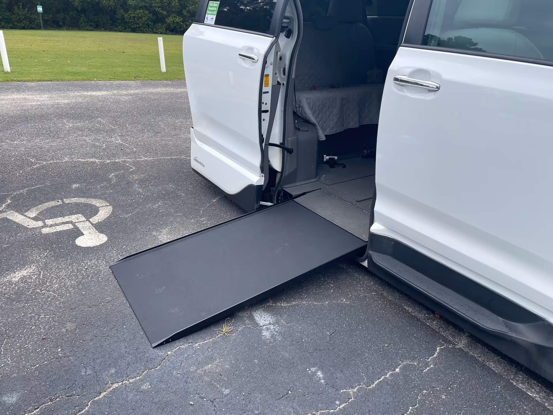 White mobility van with a deployed ramp in a parking lot.