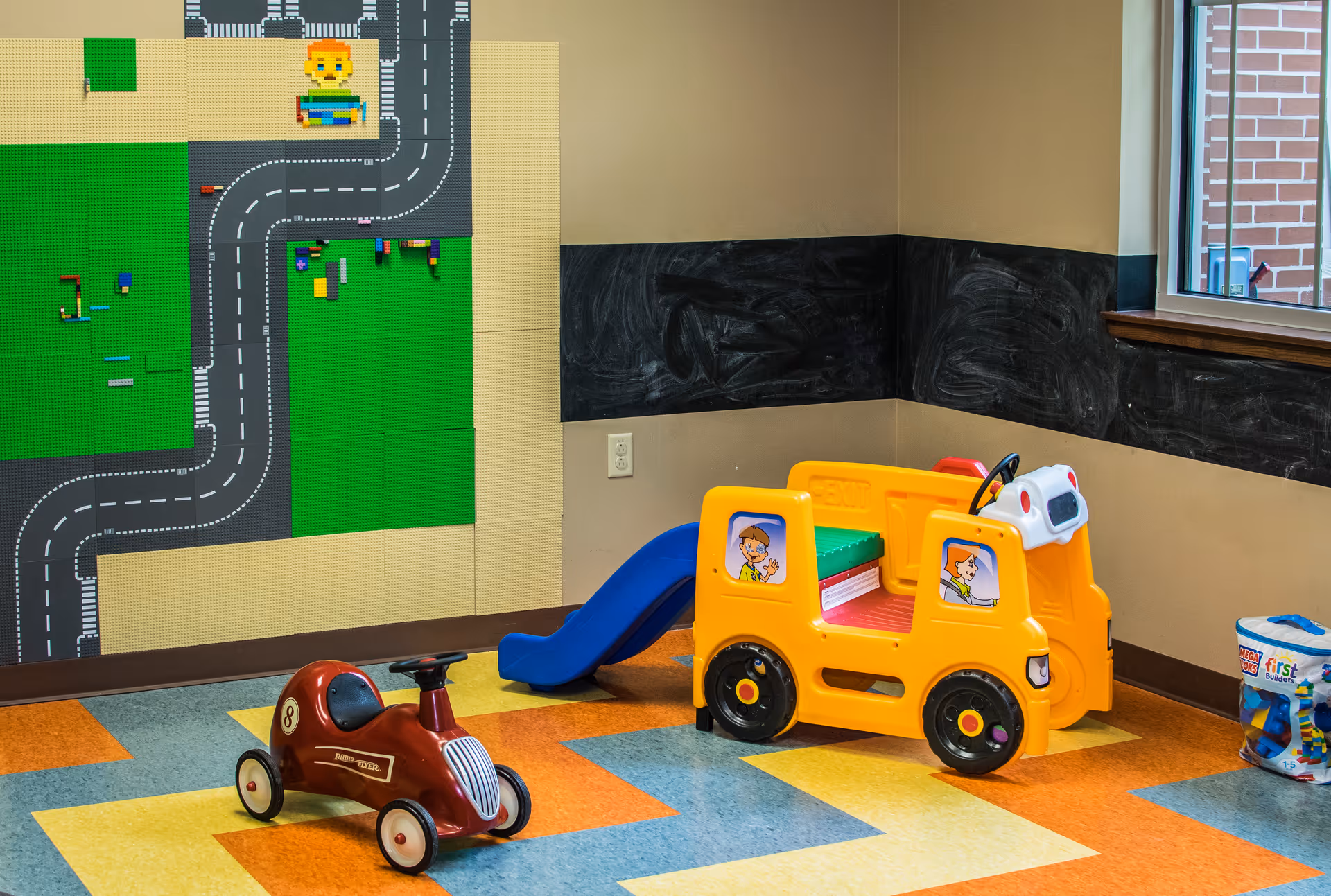 Colorful children's play area with ride-on toy cars, a slide, and a mural on the wall.