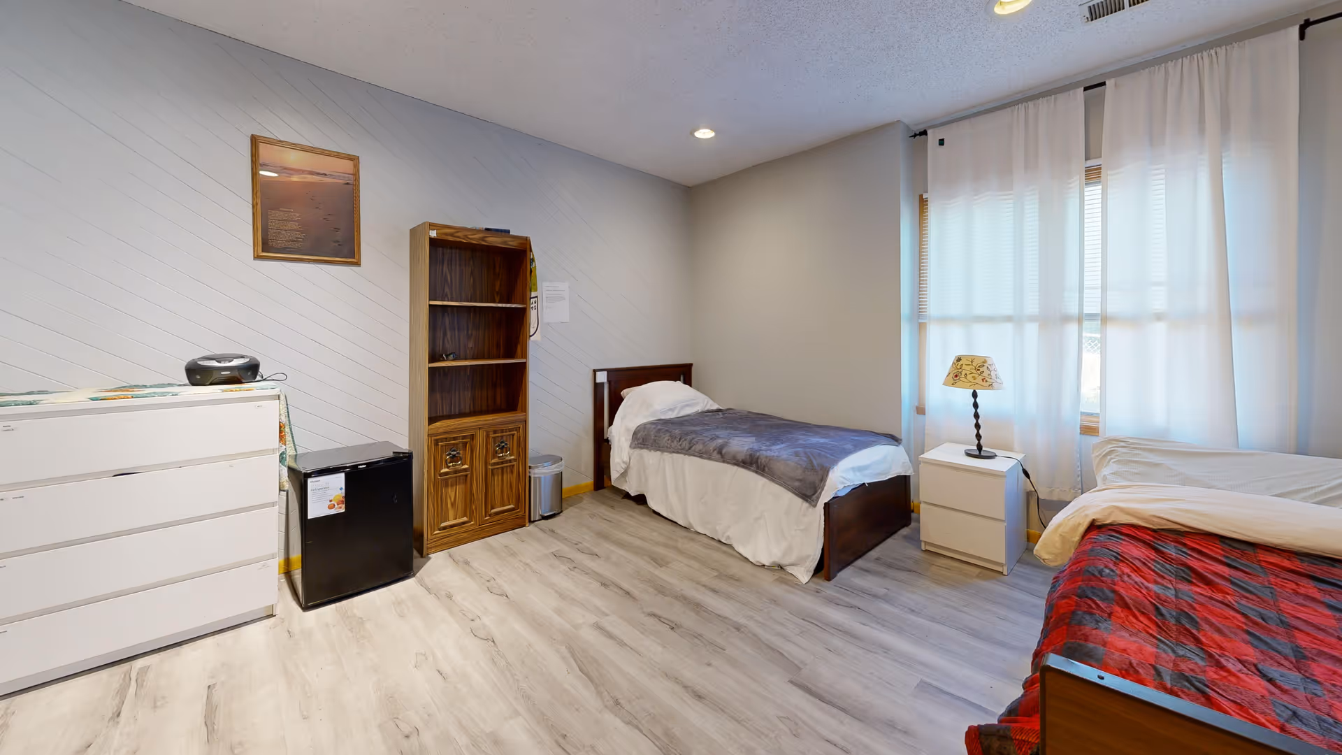 Bedroom with two beds, dresser, shelf unit, nightstand, and window.